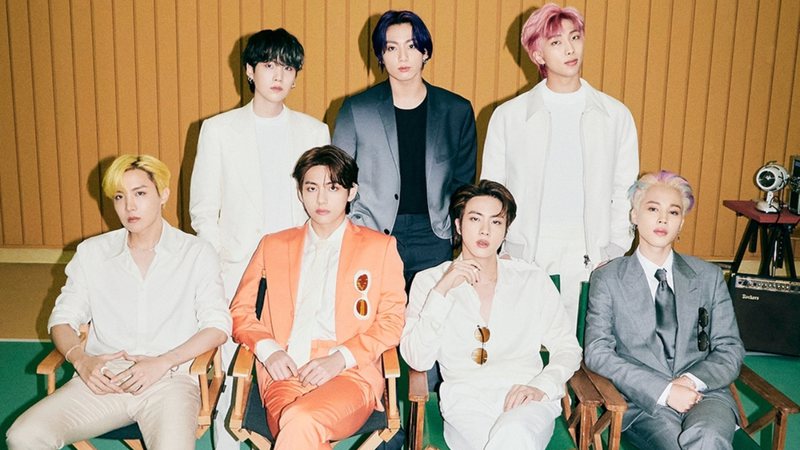 Quatro integrantes do BTS sentados em cadeiras perto um do outro; o resto do grupo posa em pé atrás dos colegas (Foto: Divulgação/Instagram)