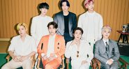 Quatro integrantes do BTS sentados em cadeiras perto um do outro; o resto do grupo posa em pé atrás dos colegas  (Foto: Divulgação / Instagram oficial)