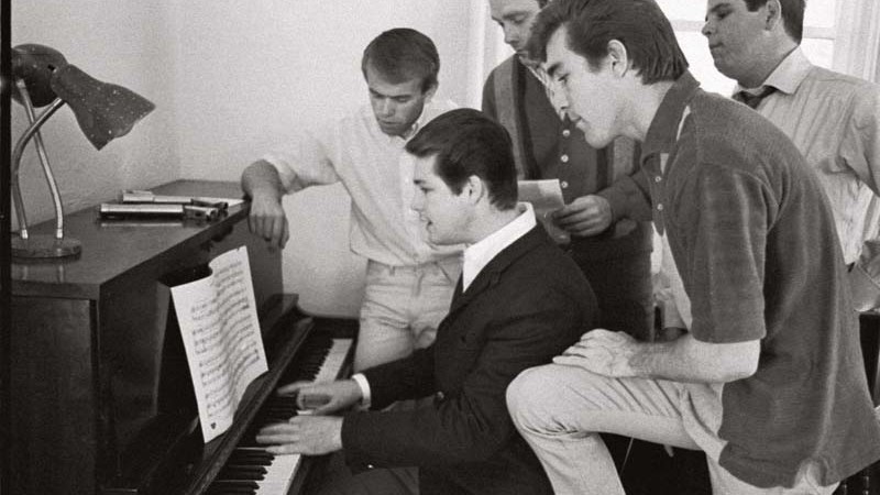 Em foto de 1964, Brian Wilson (ao piano) mostra uma nova composição para a banda. Junto a ele estão (da esq. para a dir.) Al Jardine, Mike Love, Dennis Wilson e Carl Wilson. - Divulgação