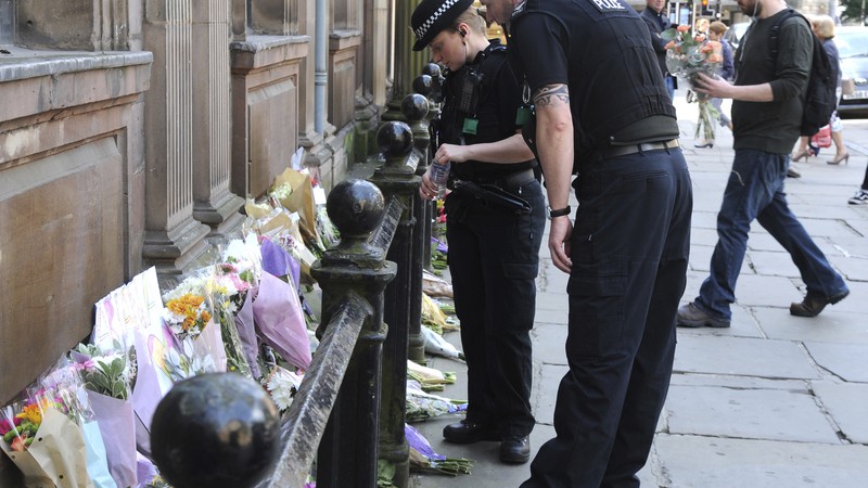 Policiais observam os tributos às vítimas do show do ataque terrorista ocorrido no show da cantora Ariana Grande em Manchester, na Inglaterra, em 23 de maio de 2017. As homenagens foram colocadas na praça St. Ann. 
