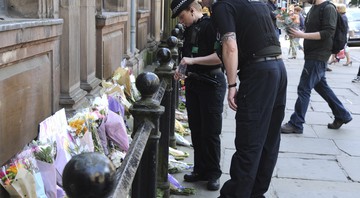 Policiais observam os tributos às vítimas do show do ataque terrorista ocorrido no show da cantora Ariana Grande em Manchester, na Inglaterra, em 23 de maio de 2017. As homenagens foram colocadas na praça St. Ann. 
 - AP