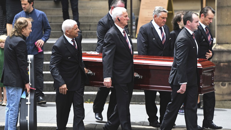 Angus Young (à esq.) segura uma guitarra enquanto o corpo de Malcolm Young, irmão dele e cofundador do AC/DC, é carregado após funeral na catedral de St Mary em Sydney, na Austrália


